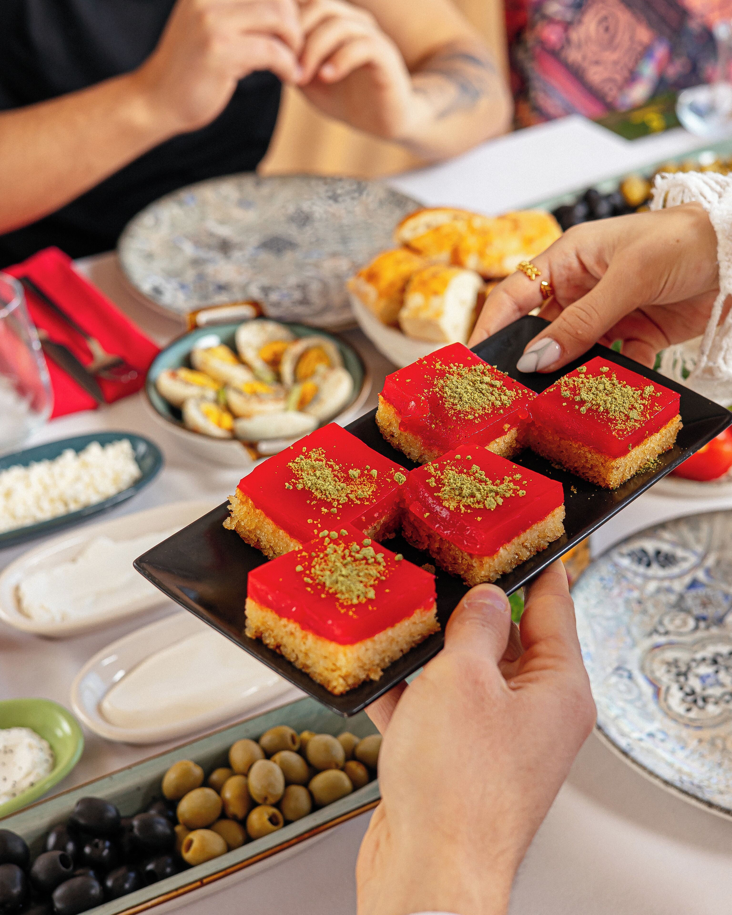A person holding a black plate with red and green dessert squares.
