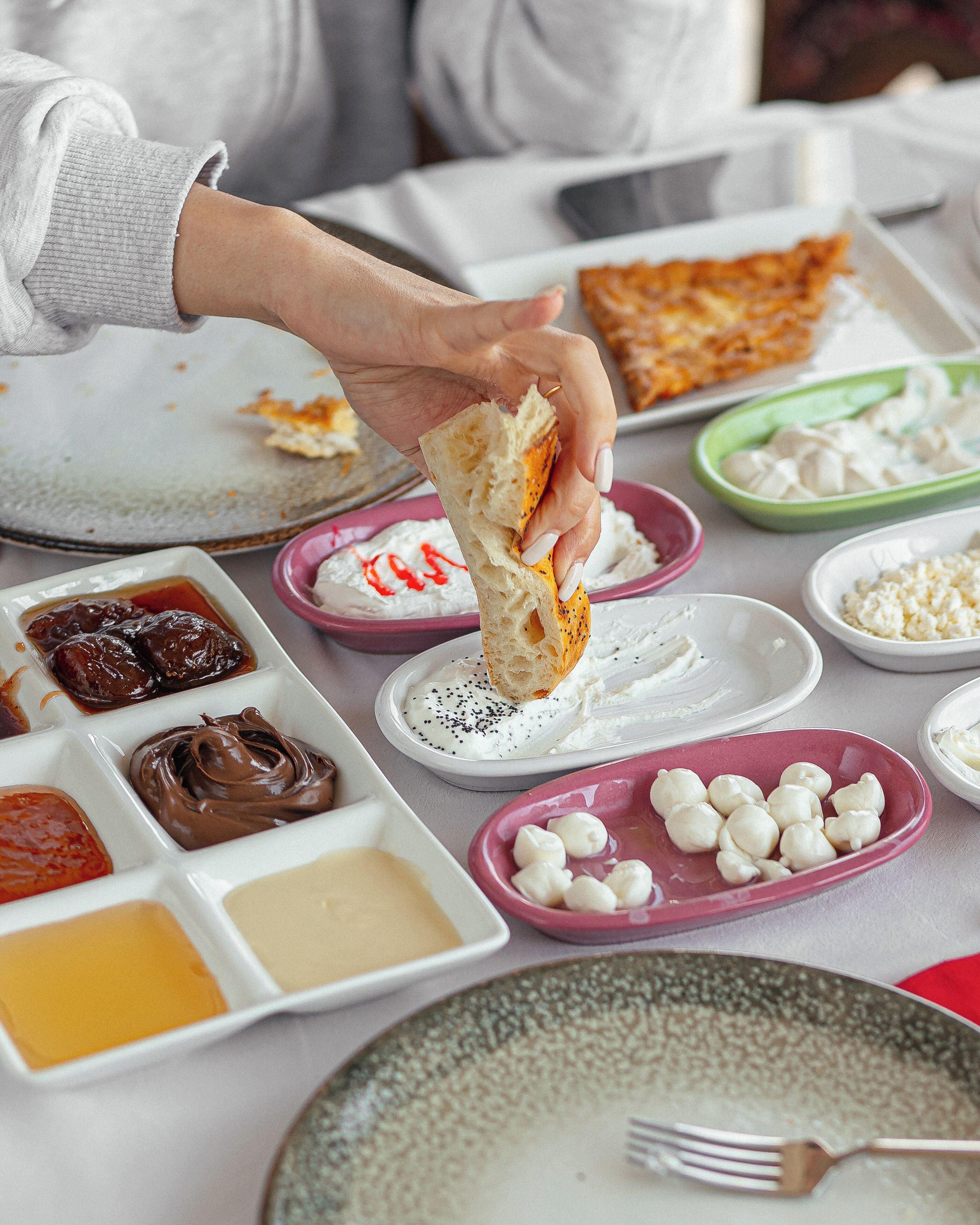 Una mesa con diferentes alimentos y una persona sosteniendo un trozo de pan.