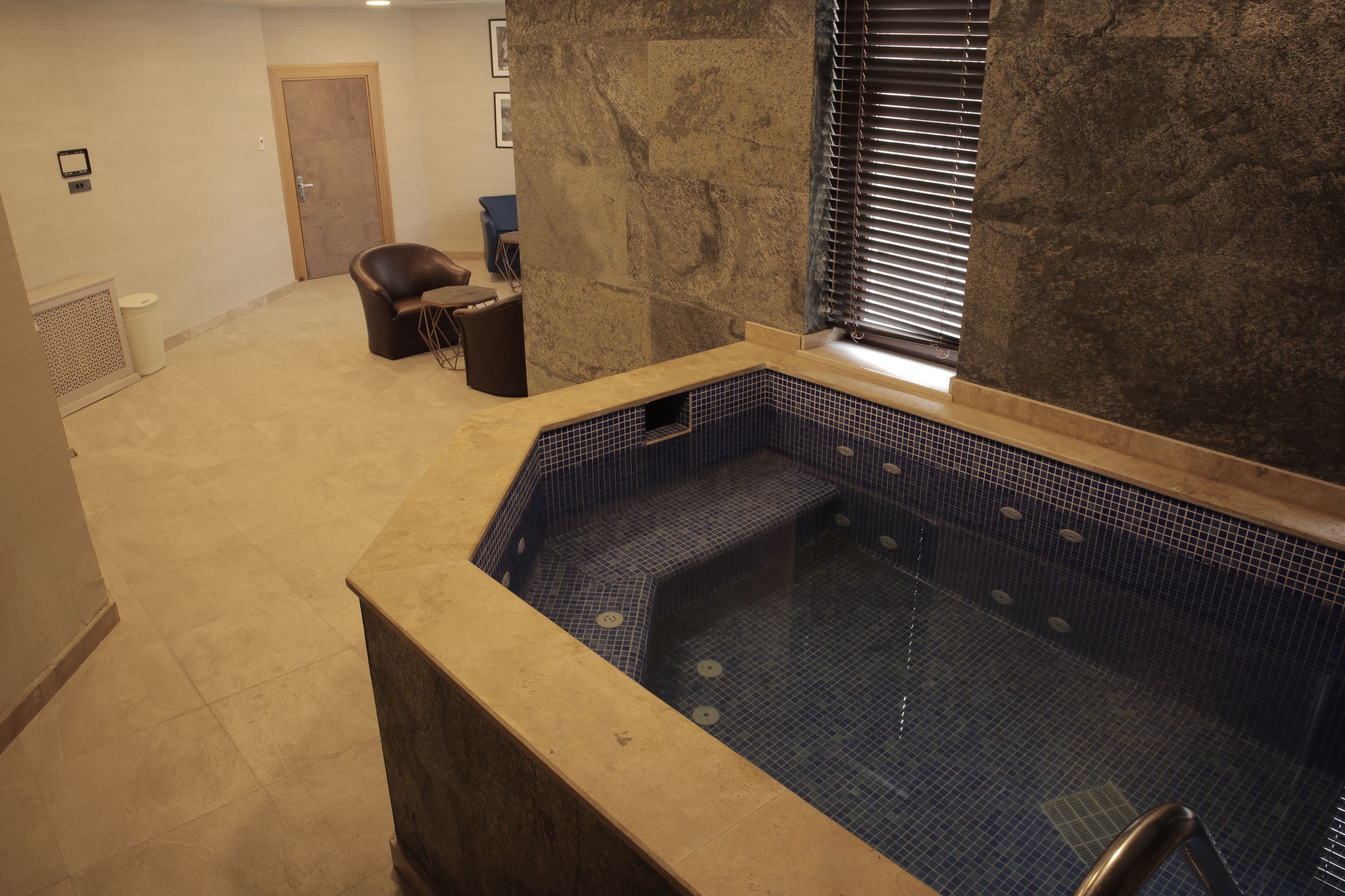 A spa area with a hot tub, a chair, and a window with blinds.