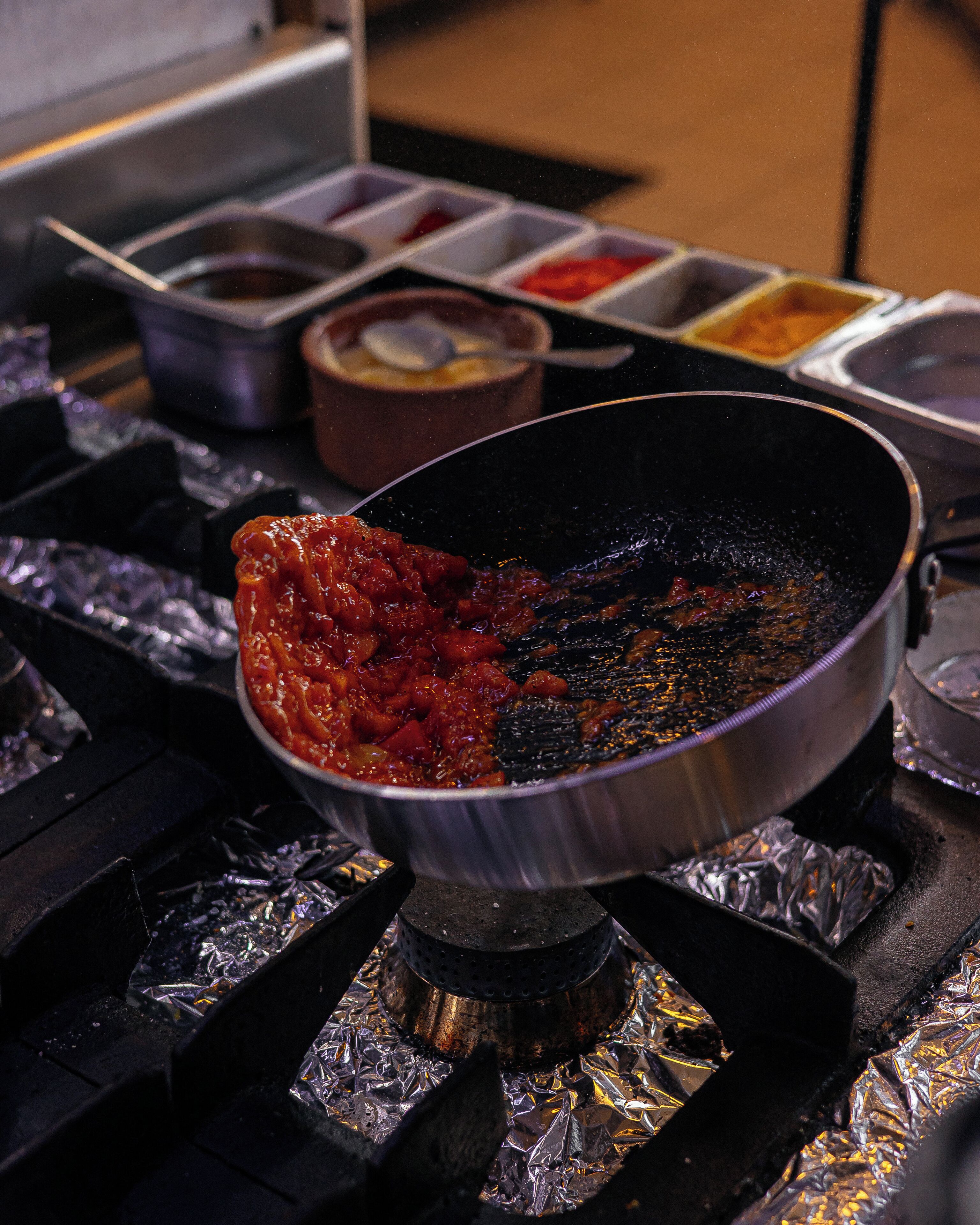 Une poêle sur une cuisinière, contenant une sauce rouge, et du papier d’aluminium placé en dessous.