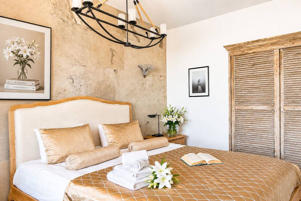 Quarto de hotel com cama, mesa de cabeceira, luminária na parede, quadro emoldurado e porta de madeira.