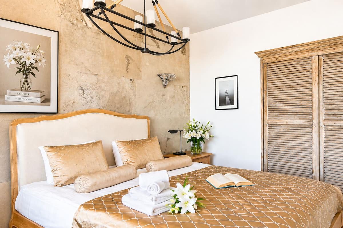 A hotel room with a bed, a nightstand, a wall-mounted light fixture, a framed picture, and a wooden door.