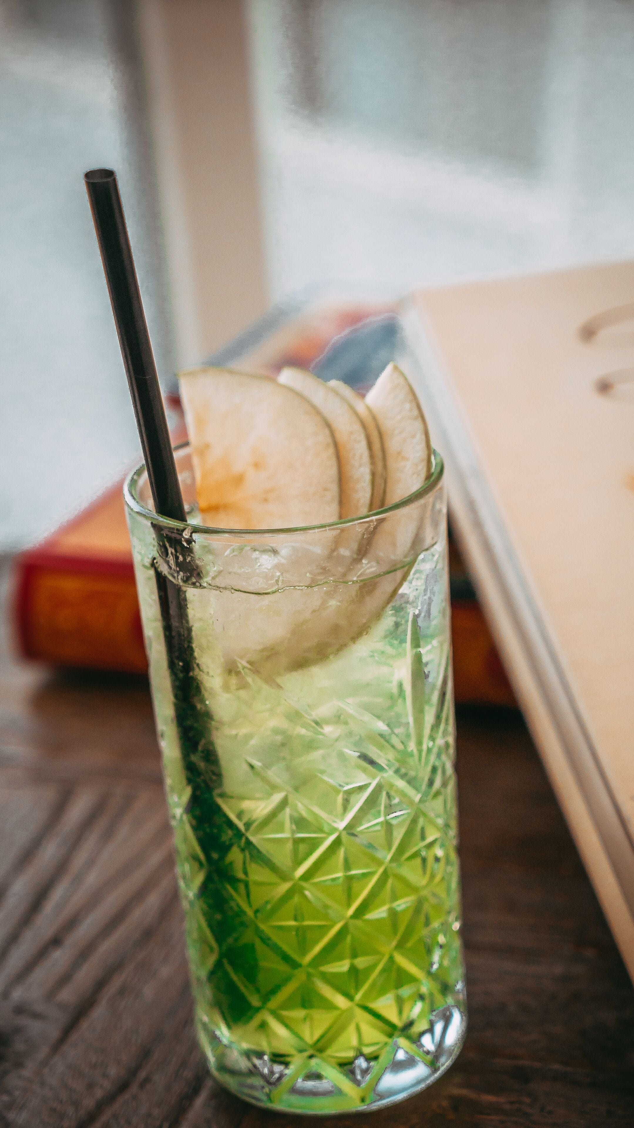 A glass with a straw and slices of apple, placed on a wooden table.