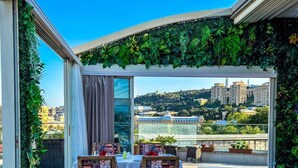 An outdoor dining area with tables and chairs, a view of a cityscape, and a green wall with plants. - Shirvanshah Hotel (Baku)