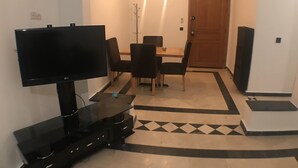 Una sala de estar con un televisor de pantalla plana, una mesa de comedor con sillas y una alfombra estampada.