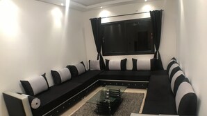 Una sala de estar moderna con un sofá seccional blanco y negro, una mesa de centro de vidrio y un ventanal con cortinas negras.