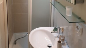 Een badkamer met een douchecabine van glas, een wit toilet en een spiegel met verlichting erboven.