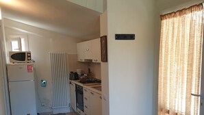 Een keuken met een raam, een radiator en een klein raam boven de gootsteen.