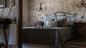 Um quarto com parede de pedra, uma cama com almofadas, uma mesa de cabeceira e uma luminária fixada na parede.