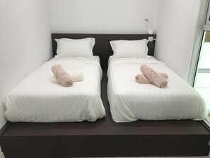 Two single beds with white mattresses and matching pillows, each with a bedside table and lamp.