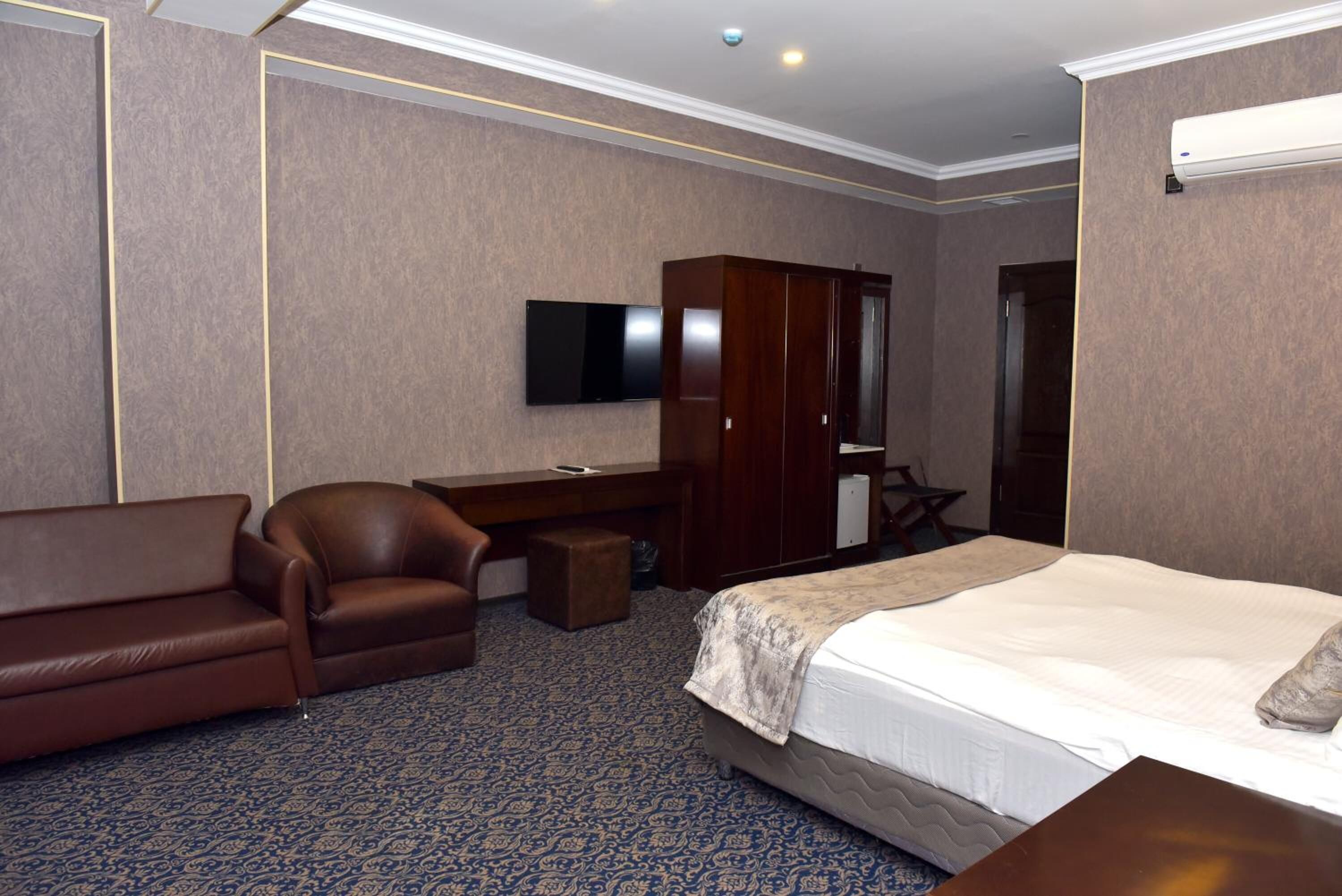 A hotel room with a bed, a brown leather sofa, a wooden desk, a television, and a wardrobe.
