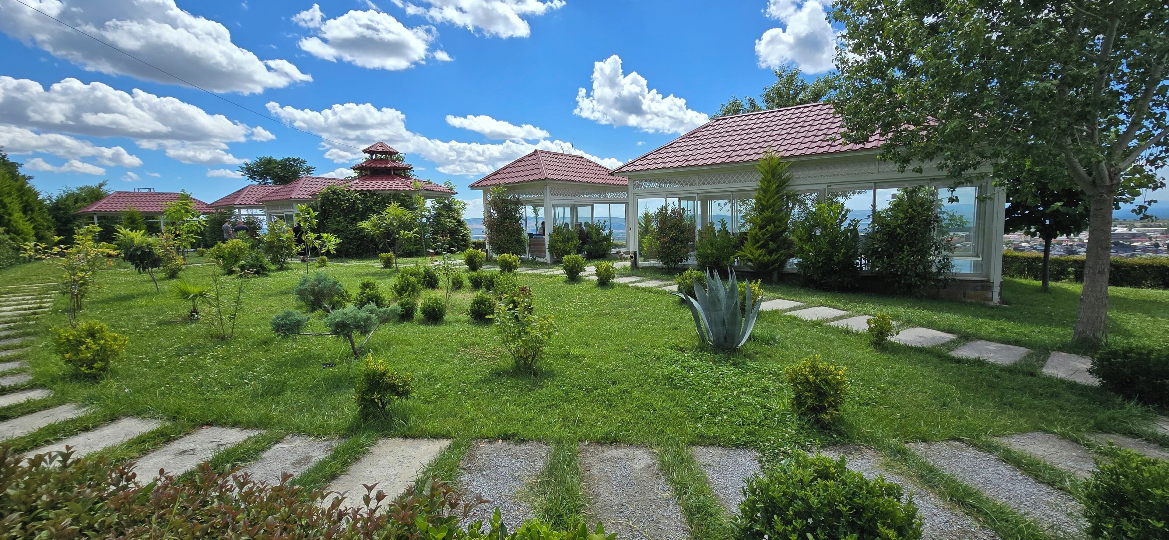 Un jardín con un pabellón, una construcción al estilo pagoda y una estructura blanca con techo rojo.
