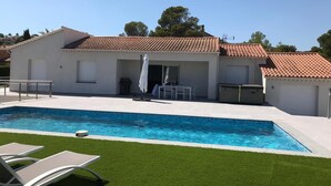 Ein modernes Haus mit Swimmingpool, einer Terrasse mit Sitzgelegenheiten und einem kleinen Garten.