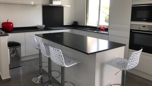 Eine moderne Küche mit einer großen Kochinsel, Edelstahl-Barhocker und einem roten Apfel auf der Arbeitsplatte.