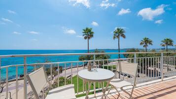 Un balcón con dos sillas y una mesa, con vista a una playa con palmeras y el mar.