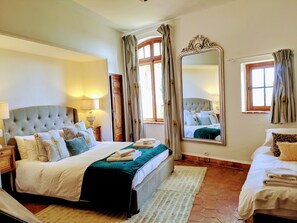 A well-lit bedroom with a large bed, a nightstand, a mirror, and a window with curtains.