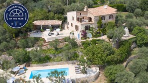 A stone villa with a swimming pool, surrounded by lush greenery and olive trees.