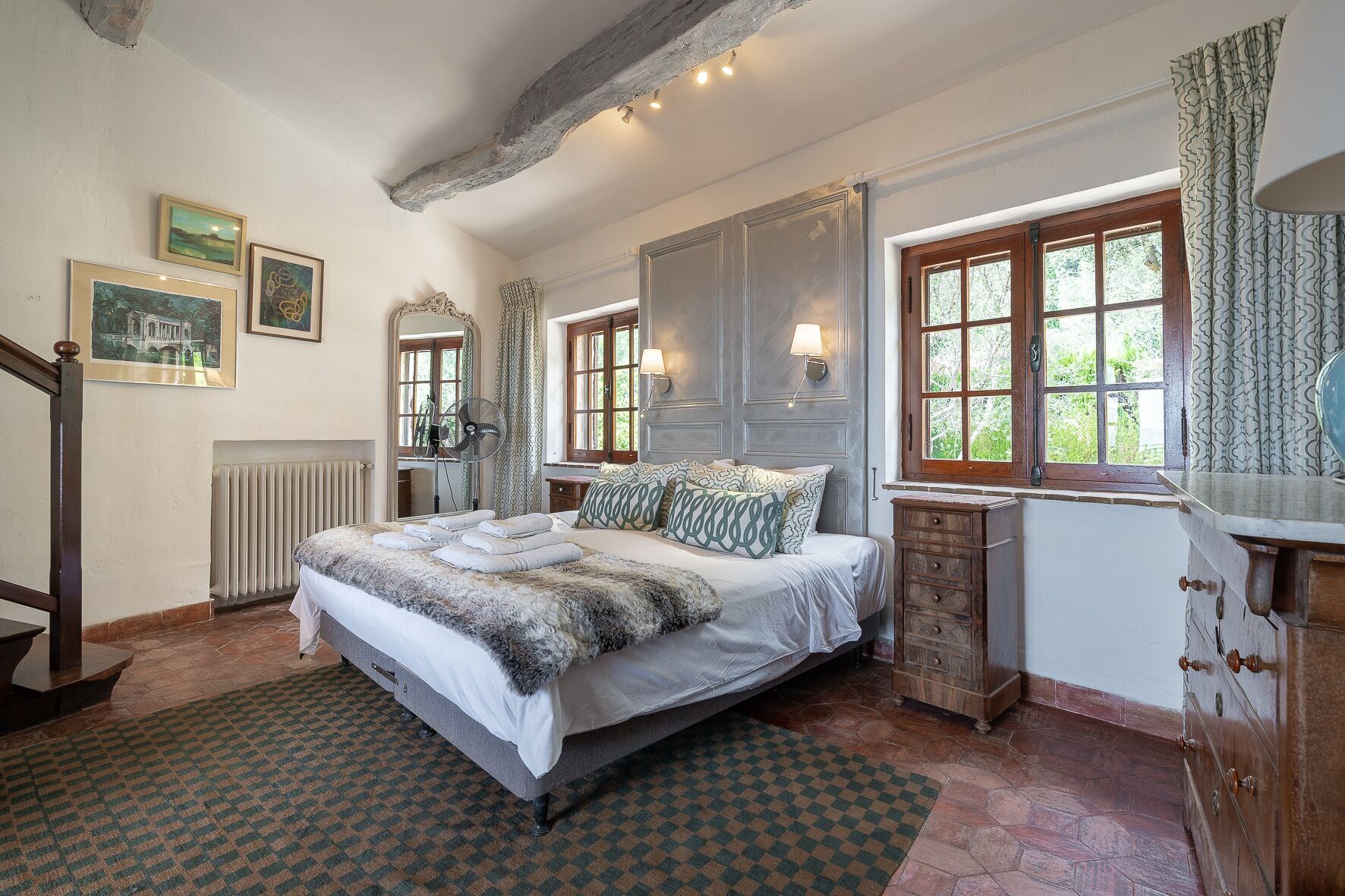 A bedroom with a bed, a dresser, a mirror, a radiator, and a window with curtains.