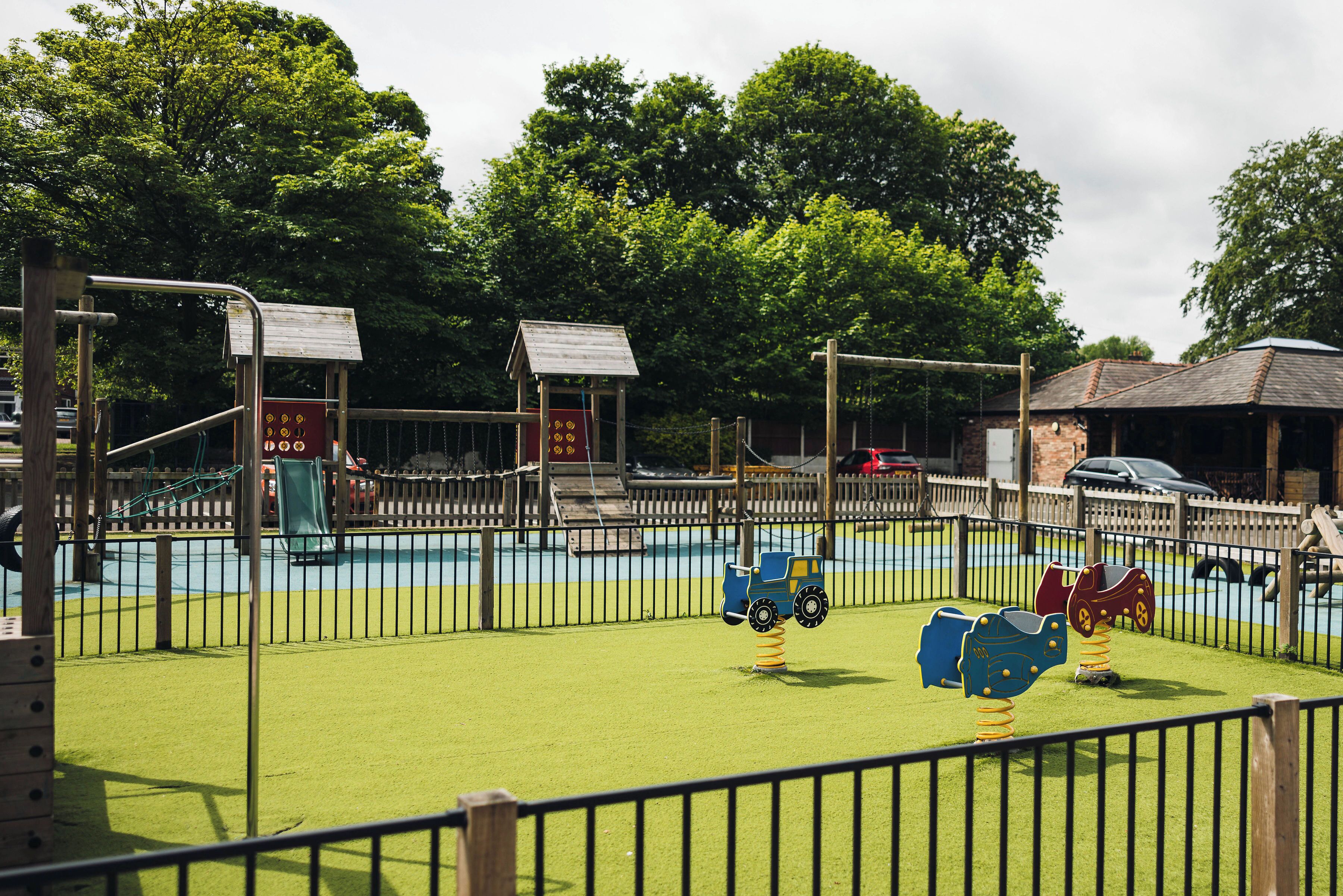 A playground with a fenced area, swings, and a small building structure.