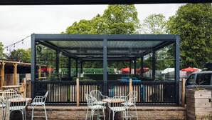 An outdoor seating area with tables and chairs, a covered patio, and a view of the surrounding trees. - Griffin Inn (St Helens)