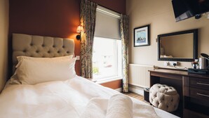 A hotel room with a bed, a window with curtains, a dresser, a mirror, and a television. - Griffin Inn (St Helens)