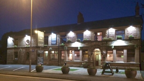 A stone building with multiple windows and a central entrance. There are potted plants on the ground level and a signboard on the left side. - Griffin Inn (St Helens)