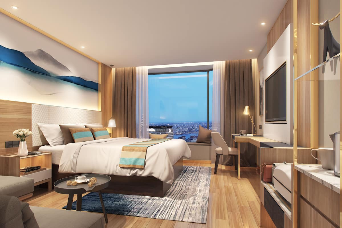 A modern hotel room with a large bed, a desk, a TV, and a view of the cityscape.