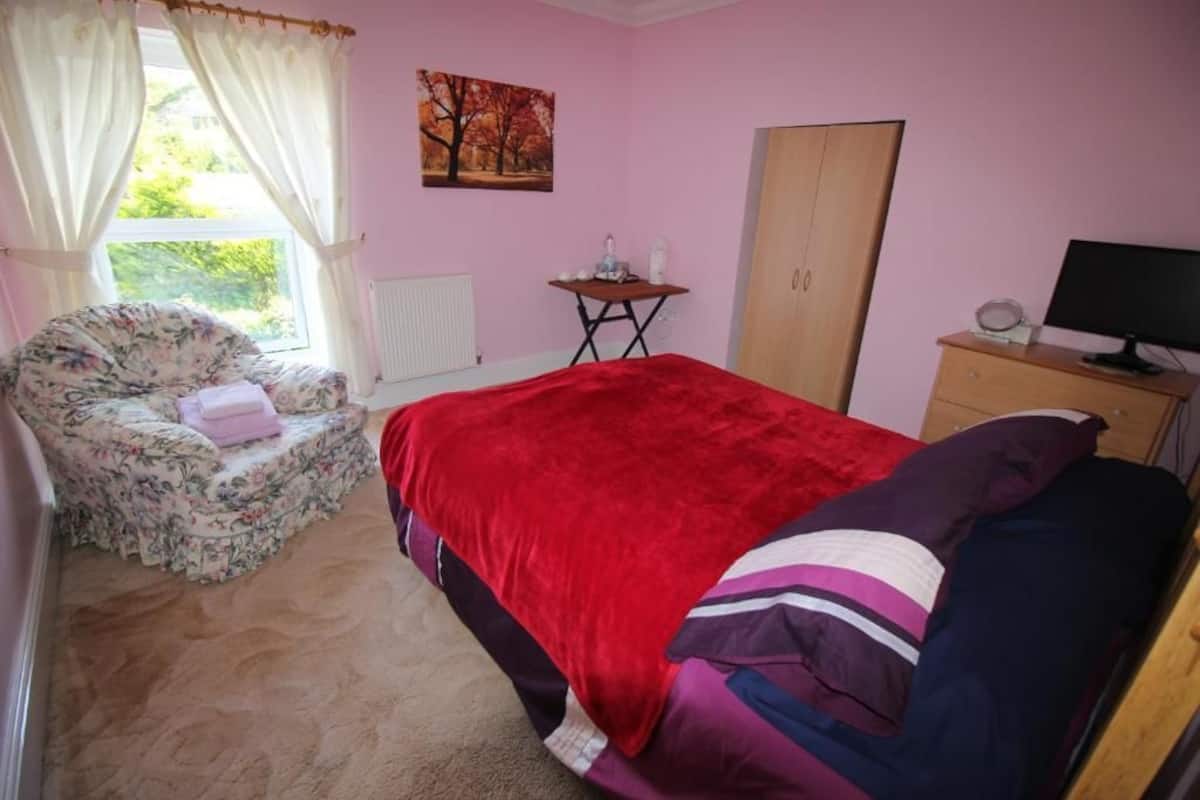 Un dormitorio con cama, una silla, un escritorio y un armario.