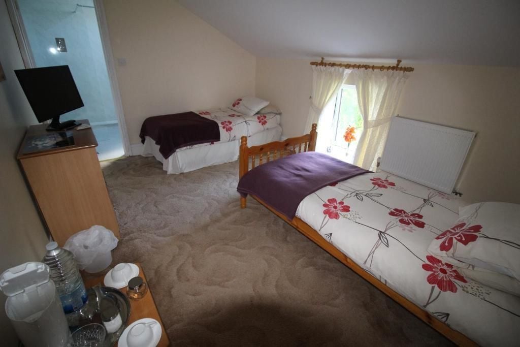A bedroom with two beds, a desk with a computer, and a window with curtains.