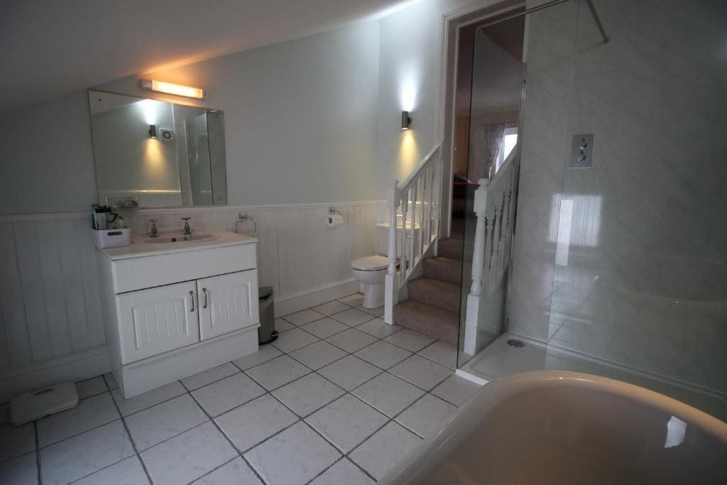 Bagno con mobiletti bianchi, un WC, zona doccia e una scala che conduce in un'altra stanza.