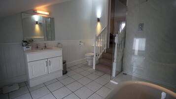 Un baño con tocador blanco, inodoro, zona de ducha y una escalera que lleva a otra habitación.