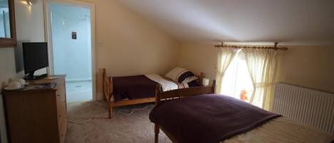 A bedroom with two beds, a dresser, a desk with a computer, and a window with curtains.