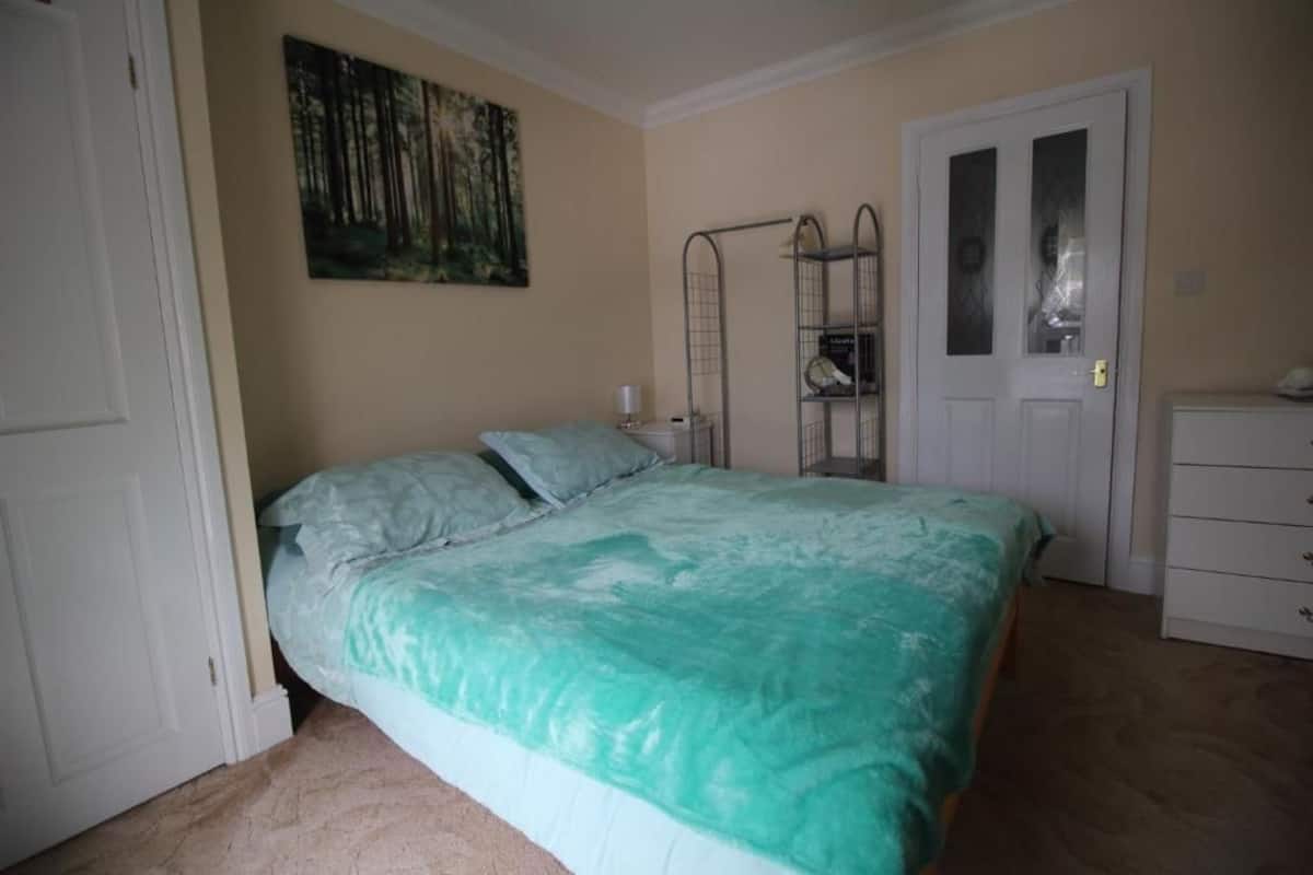 Un dormitorio con cama, una puerta, un aparador blanco y una estantería metálica.