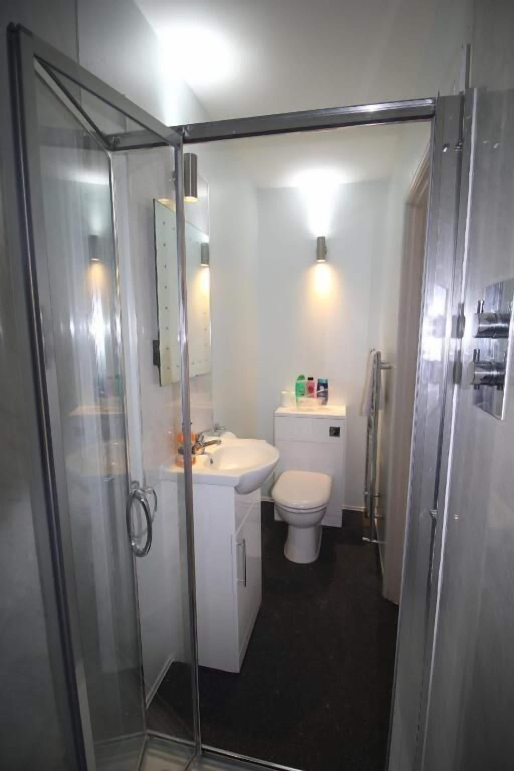 Un baño pequeño con cabina de ducha de vidrio, un lavamanos blanco y un inodoro.
