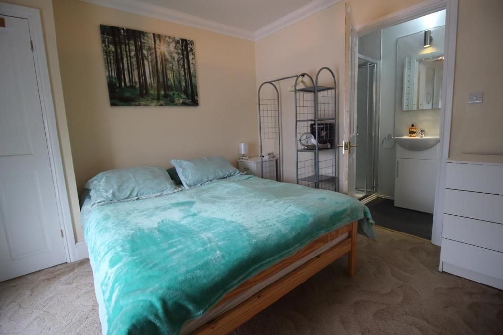 A bedroom with a bed, a painting, a metal rack, and a bathroom visible through an open door.