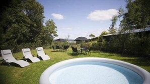 Una piscina exterior con sillones de descanso y sombrillas, rodeada de vegetación y un cielo despejado.