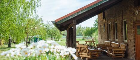 Ein rustikales Gebäude mit überdachter Terrasse, Holzmöbeln und einem Garten mit weißen Blüten.