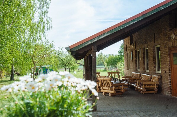 A rustic building with a covered patio area, wooden furniture, and a garden with white flowers.