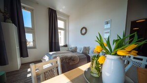 Camera d'albergo con un letto, un tavolo da pranzo, un vaso bianco con fiori e vista sull'esterno.
