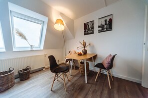 A room with a dining table, two chairs, a lamp, a vase with dried plants, a basket, and a radiator.