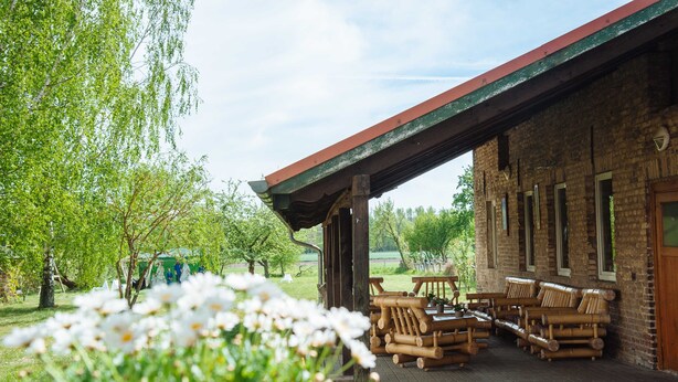 Un edificio rustico con un patio coperto, mobili in legno e un giardino con fiori bianchi.