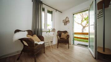 Ein Zimmer mit zwei Korbstühlen, einem kleinen weißen Tisch und einem Fenster mit Vorhängen.