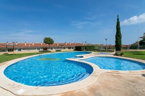 Ein Pool mit geschwungenem Design, umgeben von einer gepflasterten Fläche und einer Reihe von Gebäuden mit roten Ziegeldächern.
