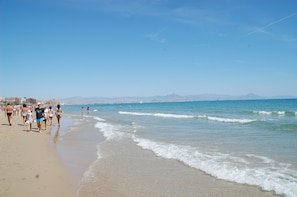 A beach with people walking along the shore, a clear sky, and distant mountains. - APARTMENT NEAR THE BEACH (Gran Alacant)