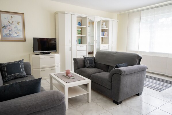 A modern living room with a grey sofa, a white coffee table, and a television on a white cabinet.