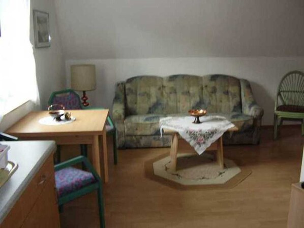 Une pièce comprenant une table en bois, une chaise verte, un canapé et une petite table recouverte d’une nappe.