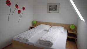 Une chambre à coucher avec un lit, deux tables de chevet, une petite table, un tableau encadré au mur et trois fleurs rouges.