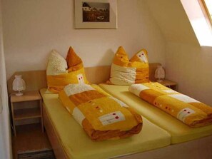 Een kamer met twee bedden, een lijst aan de muur en een nachtkastje met een lamp.
