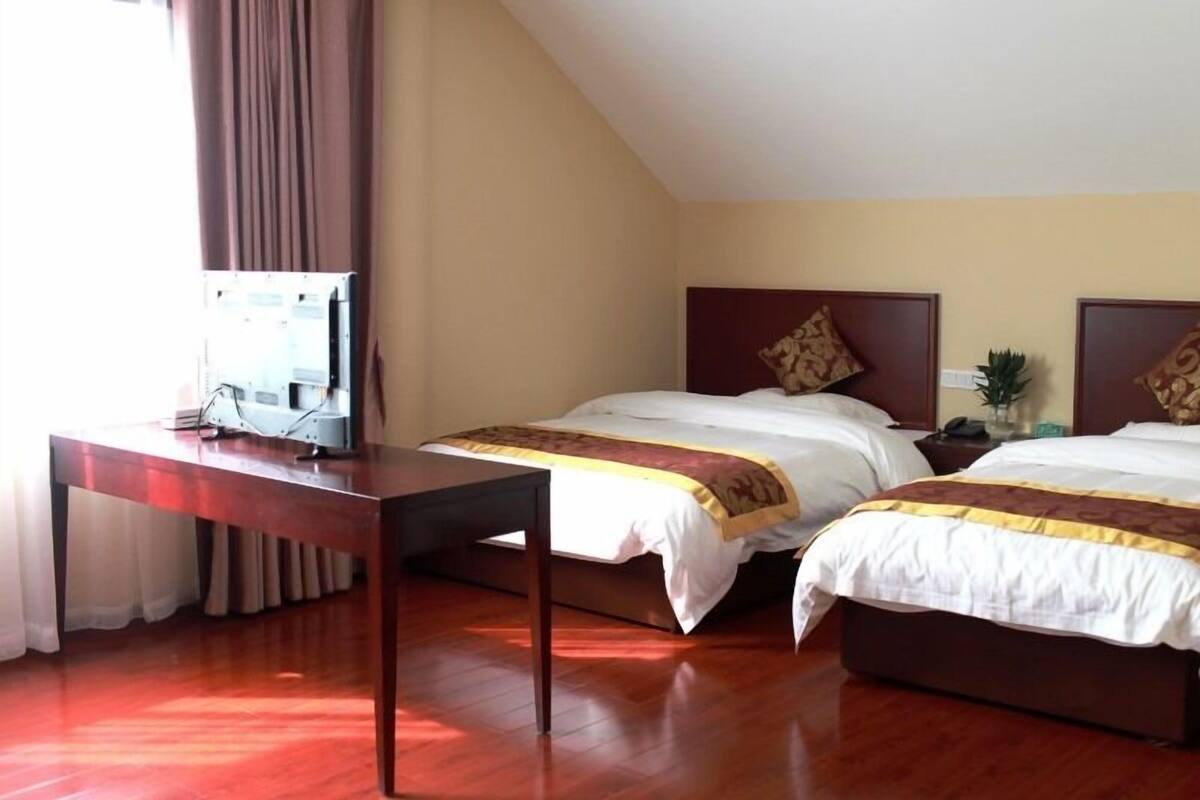 A hotel room with two beds, a wooden desk, and a television.