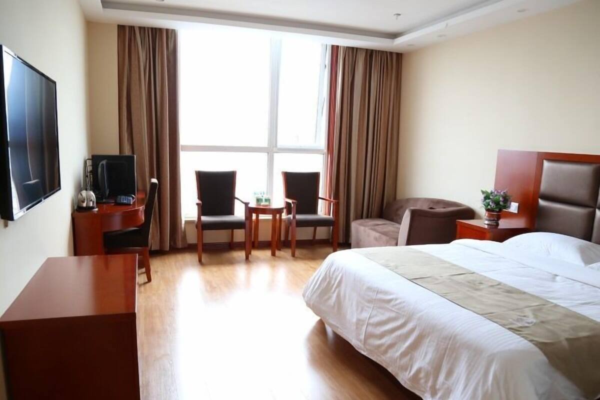 Une chambre d’hôtel avec un lit, un bureau avec une télévision, deux chaises, une petite table et une fenêtre avec des rideaux.